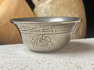 These offering bowls are metal finished with silver plate. They are decorated with repeating etched rim and flower medallions. From Nepal. These make beautiful miniature offering bowls and when filled with sand are perfect for holding incense. Measurements: 3 cm height, diameter at top 6 cm