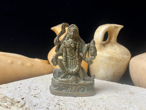 Kali with four arms, standing on Shiva, holding a curved sword, severed head and skull cup. Her fourth hand displays the gesture of blessing. She wears a garland of skulls around her neck and is covered by her long, wild, disheveled hair. This statue is approximately 80 years old (early 20th century). She has a fine and evenly dark patina. Measurements: height 7.3 cm, width 5 cm.