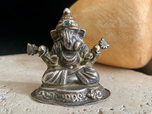 Small vintage Ganesh statue cast in silver, with right hand up in the gesture of protection and left hand holding his favourite ladoo sweet. His other hands hold lotus flowers. Lightweight but very finely cast with a small facet cut blue topaz in his forehead. 50 years old, southern India. 5 cm height