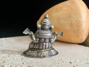 Small vintage Ganesh statue cast in silver, with right hand up in the gesture of protection and left hand holding his favourite ladoo sweet. His other hands hold lotus flowers. Lightweight but very finely cast with a small facet cut blue topaz in his forehead. 50 years old, southern India. 5 cm height
