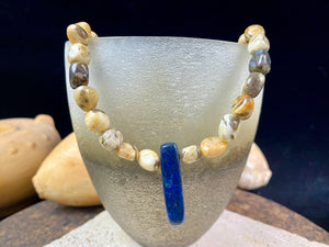 A necklace crafted from zebradorite jasper with highlight beads of grey opal and a central hand carved pendant of Afghani lapis lazuli. Finished with sterling silver beads and hook clasp. Our necklace can be worn by either men or women Length 42.4 cm