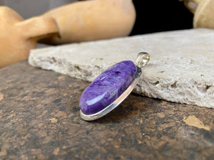 This lustrous charoite pendant is set off by a sterling silver bezel, topped by a bail that’s large enough to accommodate a thick chain or cord. A stunning piece of purple charoite with deep colour.  Measurements: 5.2 cm (2 in) height including bail, 2.2 cm (0.75 in) at widest point 
