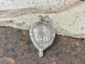 This amulet depicts Durga within the framework of the yoni leaf shape. High grade silver. Early 20th century or older. The double bail has an original wrap of cotton cord over it to protect it from further wear. Wear to the bail is evident but remains sturdy.  Measurements: height 5.5 cm including bail, width 3.4 cm