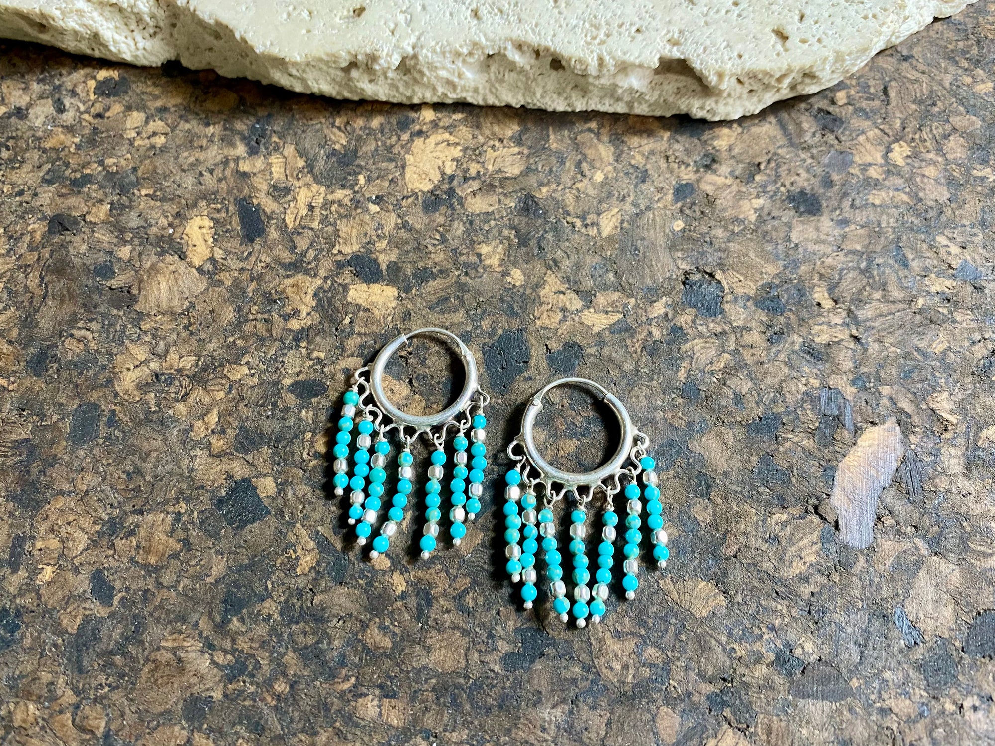 Our handmade fringed southwest-style turquoise earrings are crafted from Sleeping Beauty turquoise and handmade silver bead detailing. Sterling silver hoops complete the look. These earrings are designed to sit with the fringe facing parallel to the face. Measurements: Length 3.7 cm, 2 cm diameter