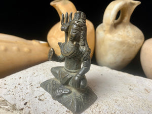 A small cast brass Shiva in serene seated style. This piece has some rubbing on the right hand side of the face and displays softened edges from decades of handling. It has a naturally darkened patina and is approximately 80 years old, or older. Gujarat, India. Measurements: Height 7.7 cm x width 5 cm x depth 3.5 cm