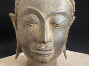Thai Buddha head. Serene expression, hair topped with the flamed Ushnisha. Sukhothai style, bronze, mid 20th century. A softly contoured face with the bow shaped lips, prominent ears, arched eyebrows and aristocratic features typical of this style of work. Measurements: height 25 cm, width 11 cm