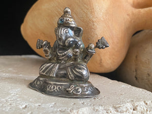 Small vintage Ganesh statue cast in silver, with right hand up in the gesture of protection and left hand holding his favourite ladoo sweet. His other hands hold lotus flowers. Lightweight but very finely cast with a small facet cut blue topaz in his forehead. 50 years old, southern India. 5 cm height