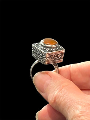 An unusual ring featuring a round carnelian stone set in a high box setting. Afghanistan, mid to late 20th century. Can be worn by either men or women. Measurements: Ring face 2.5 x 2.5, cm, height 1.5 cm. This is an adjustable ring spanning sizes 7 - 8