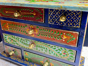 Hand painted chest of drawers features six drawers of varying sizes. Petite feet and polished brass knobs as handles. Small and compact, it is an ideal choice for storing a variety of items. Width 24 cm, depth 10 cm, height 17.5 cm
