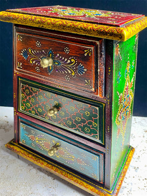 This intricately hand painted box features three drawers and small feet. Brass knobs as handles add a touch of elegance, perfect for holding everything from trinkets to jewellery. Width 21.5, depth 11.5 cm, height 24 cm
