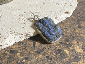 Hand carved square labradorite pendant depicting Ganesh, elephant headed god of wisdom, prosperity and new beginnings. This is a unique and individual piece, hand carved by an artisan in Jaipur, with a light blue luminosity that changes depending on the angle of lighting. Sterling silver frame and bail. The bail is generous enough to allow a large chain or cord to pass through.  This unisex labradorite pendant will suit both men and women.  Measurements: height 4.7 cm including bail, width 3 cm