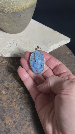 Hand carved labradorite pendant depicting Ganesh, elephant headed god of wisdom, prosperity and new beginnings. This is a unique piece, a smaller oval pendant that has a very attractive deep blue luminosity that comes alive depending on the angle of lighting. Sterling silver frame and bail. The bail is generous enough to allow a large chain or cord to pass through.  This unisex labradorite pendant will suit both men and women.  Measurements: height 4.9 cm including bail, width 2.7 cm