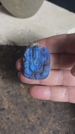 Hand carved square labradorite pendant depicting Ganesh, elephant headed god of wisdom, prosperity and new beginnings. This is a unique and individual piece, hand carved by an artisan in Jaipur, with a light blue luminosity that changes depending on the angle of lighting. Sterling silver frame and bail. The bail is generous enough to allow a large chain or cord to pass through.  This unisex labradorite pendant will suit both men and women.  Measurements: height 4.7 cm including bail, width 3 cm