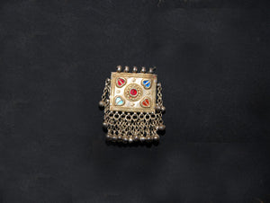 Antique Hunza Valley Uzbek pendant consisting of a flat, double skinned rectangular plaque with a central flower design surrounded by 4 stylised leaves, set with blue and red foil backed glass. Small bells hang in a fringe from the base of the pendant and the sides. Silver and faint gilding. Height 7.4 cm