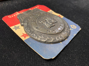 pressed tin novelty kid's police badge is still mounted on its original red white and blue display card. Made in Japan circa 1950