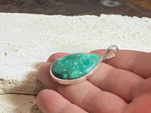 This strong green turquoise teardrop pendant is set off by a sterling silver bezel, topped by a bail that’s large enough to accommodate a thick chain or cord. Can be worn by men or women. A stunning piece of turquoise from Tibet.