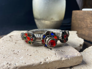 Very high grade silver, women's hinged cuff from Afghanistan. Hollow construction with a hexagon profile, this bracelet is hinged and features several florets of silver set with glass stones in red, blue and green, and a high profile reverse screw fastening and two stylised half opium poppies. 19th century