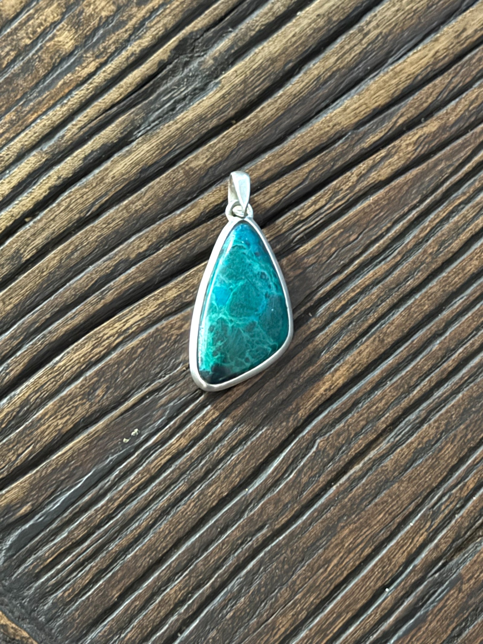 Blue green chrysocolla pendant set off by a sterling silver bezel and bail. Height 5 cm, 2.1 cm at widest point