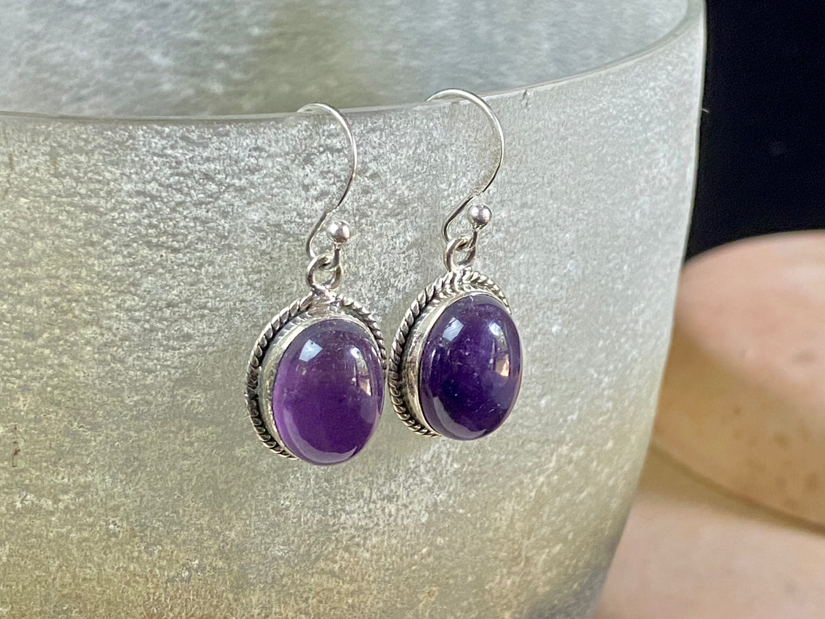 Amethyst earrings featuring high quality stones, classic darker cabochon amethysts with a detailed oval bezel. Sterling silver hook and mounts. Our amethyst earrings are open at the back to allow the natural light of the amethysts to shine through. Size 3.2 cm length including hook.