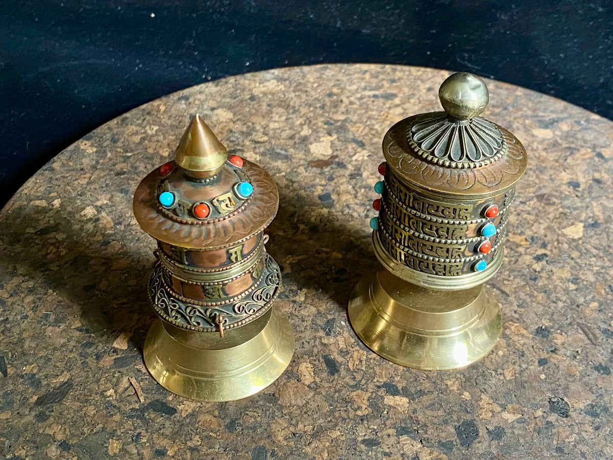 Handmade in Nepal from brass and copper, these small standing prayer wheel are weighted for spinning and contain a scroll on which is printed the mantra "Om Mani Padme Hum", a prayer to the Compassionate Buddha, written many times over. Two styles.  Measurements: height 9 cm