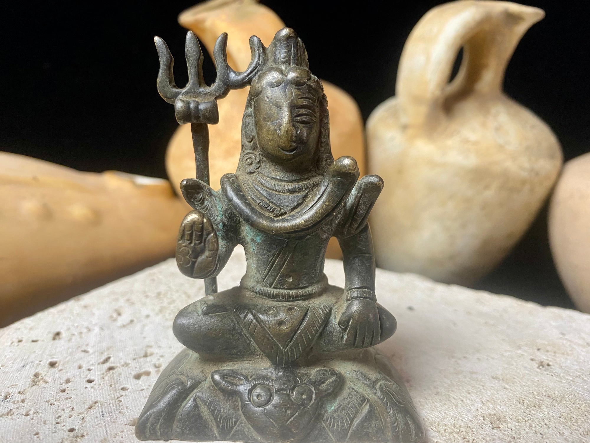 A small cast brass Shiva in serene seated style. This piece has some rubbing on the right hand side of the face and displays softened edges from decades of handling. It has a naturally darkened patina and is approximately 80 years old, or older. Gujarat, India. Measurements: Height 7.7 cm x width 5 cm x depth 3.5 cm