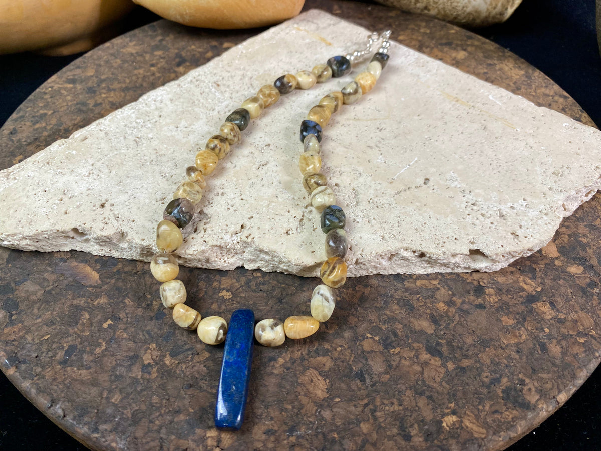 A necklace crafted from zebradorite  jasper with highlight beads of grey opal and a central hand carved pendant of Afghani lapis lazuli. Finished with sterling silver beads and hook clasp. Our necklace can be worn by either men or women  Length 42.4 cm 