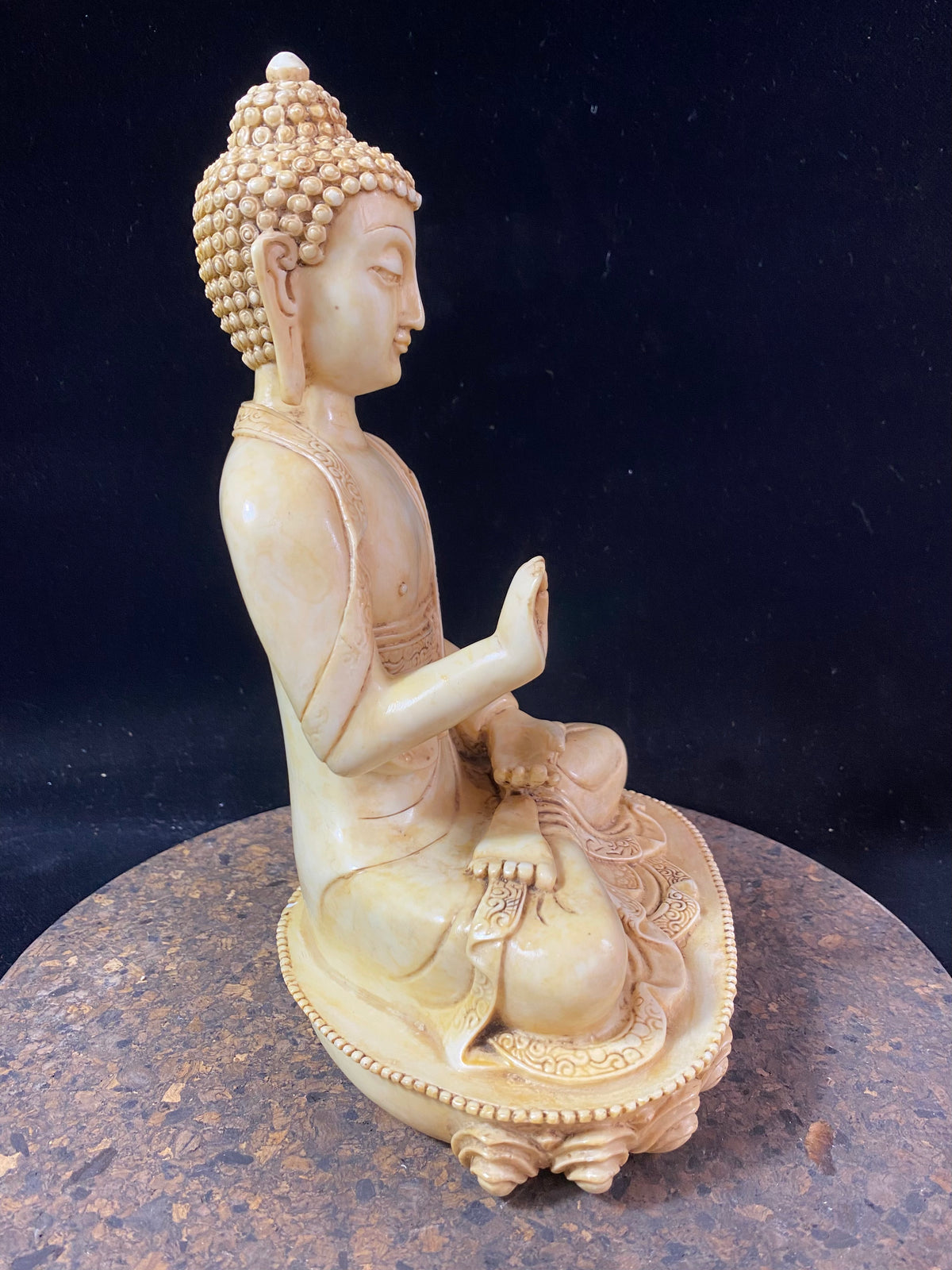 Amoghshiddhi Buddha cast in cream coloured resin. His right hand is held up facing outwards in the gesture of protection of fearlessness while his left hand sits in his lap in the gesture of meditation. Cast in solid resin, then hand finished to a very high standard. Measurements: height 26 cm, width 18 cm, depth 12 cm