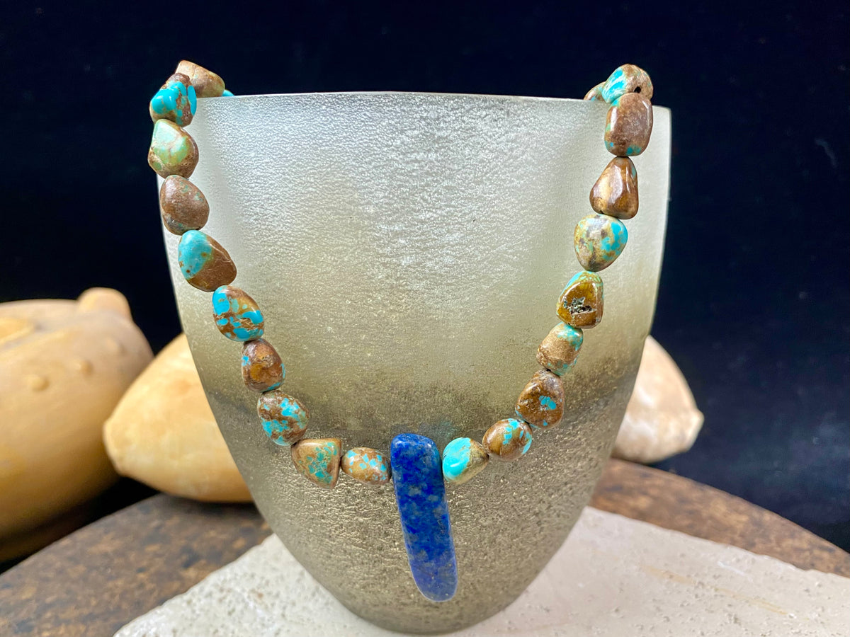 Our necklace is crafted from Tibetan turquoise with a central hand carved pendant of lapis lazuli. Finished with sterling silver beads and hook clasp. These beautiful natural stones range in colour from blue to blue-green. Length 42 cm