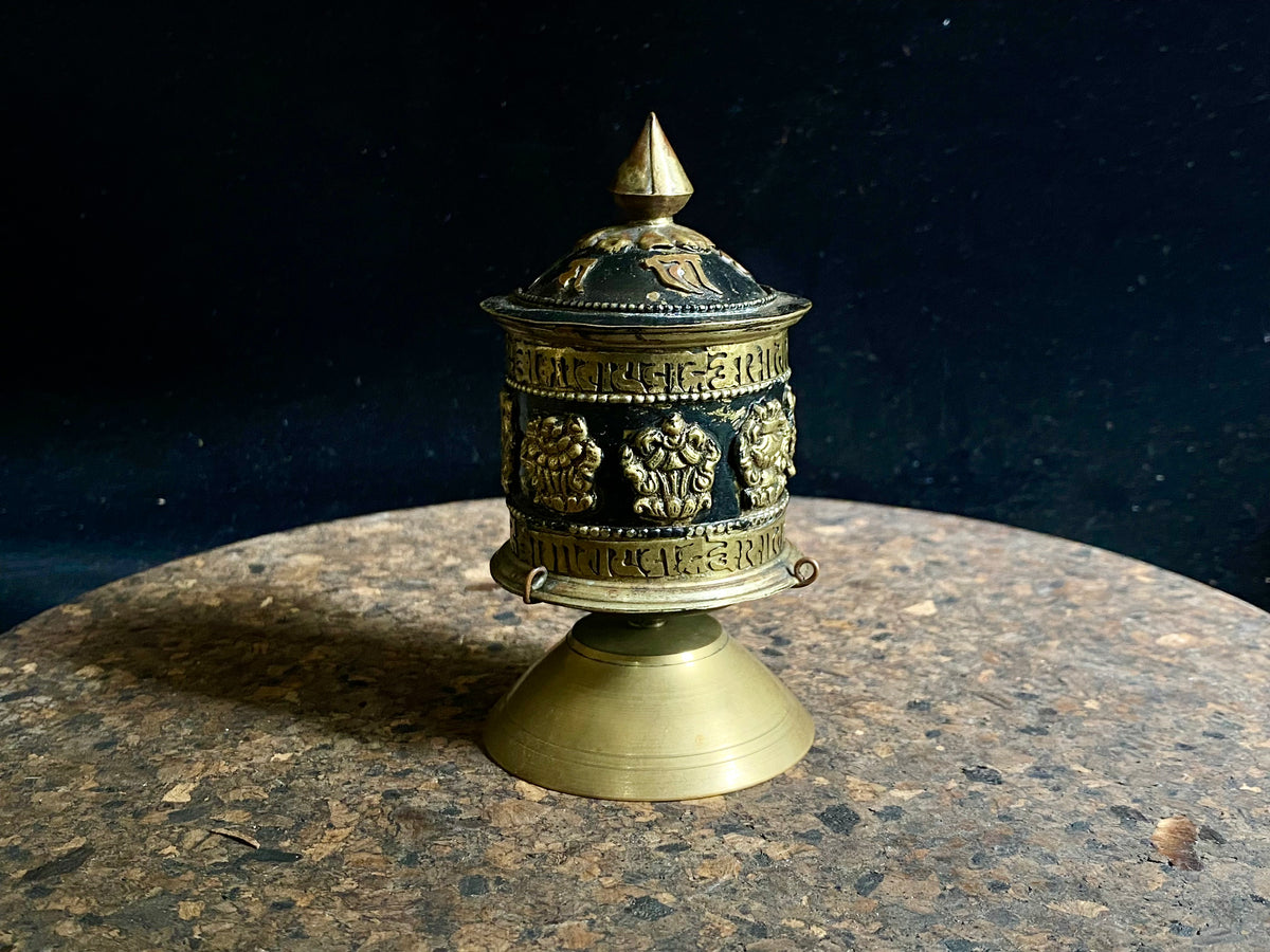 Standing prayer wheel, copper and brass, weighted for spinning and containing a scroll on which is printed the mantra "Om Mani Padme Hum", a prayer to the Compassionate Buddha, printed many times over. Measurements: height 12 cm, diameter 6.3 cm
