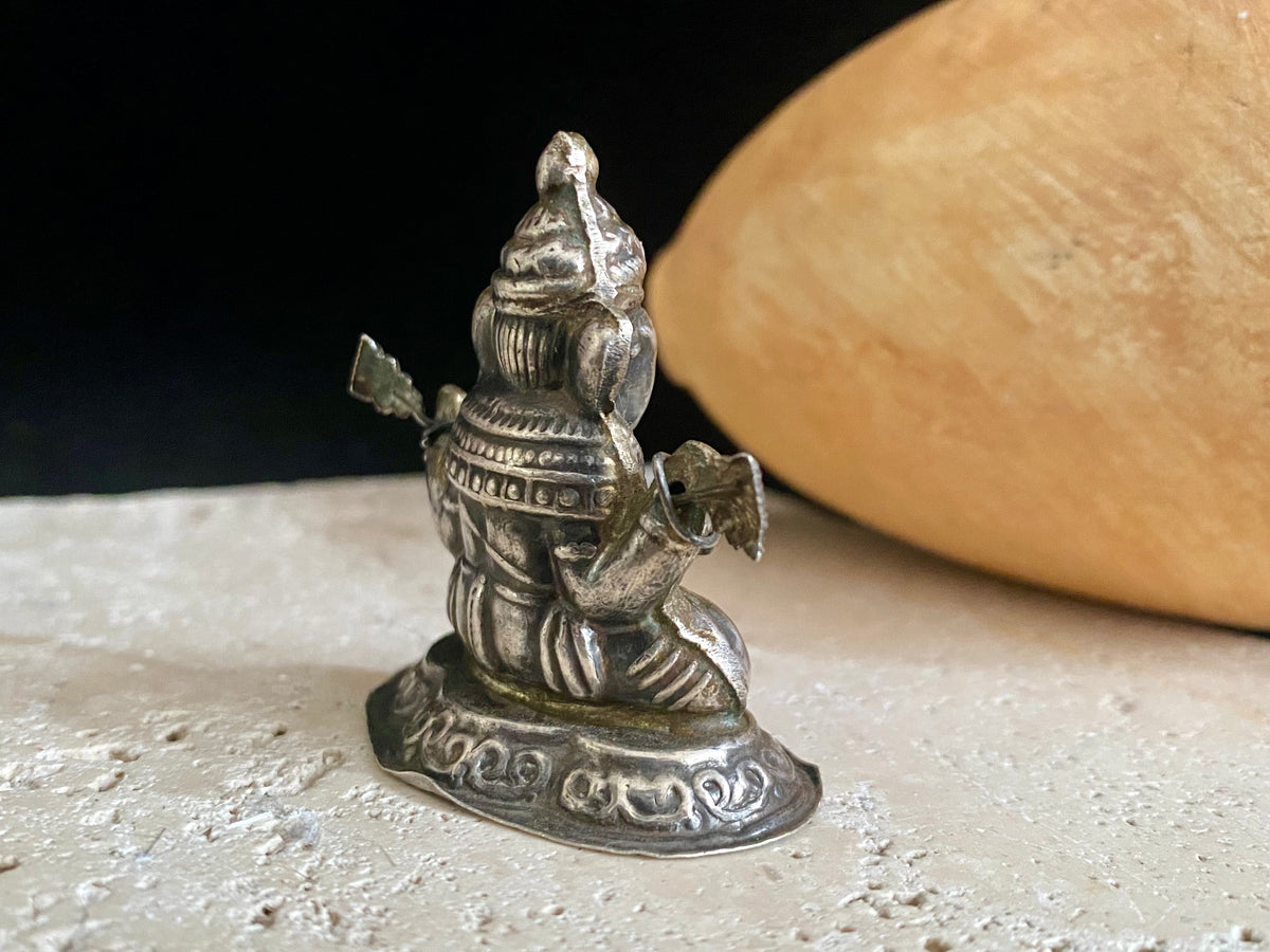 Small vintage Ganesh statue cast in silver, with right hand up in the gesture of protection and left hand holding his favourite ladoo sweet. His other hands hold lotus flowers. Lightweight but very finely cast with a small facet cut blue topaz in his forehead. 50 years old, southern India. 5 cm height