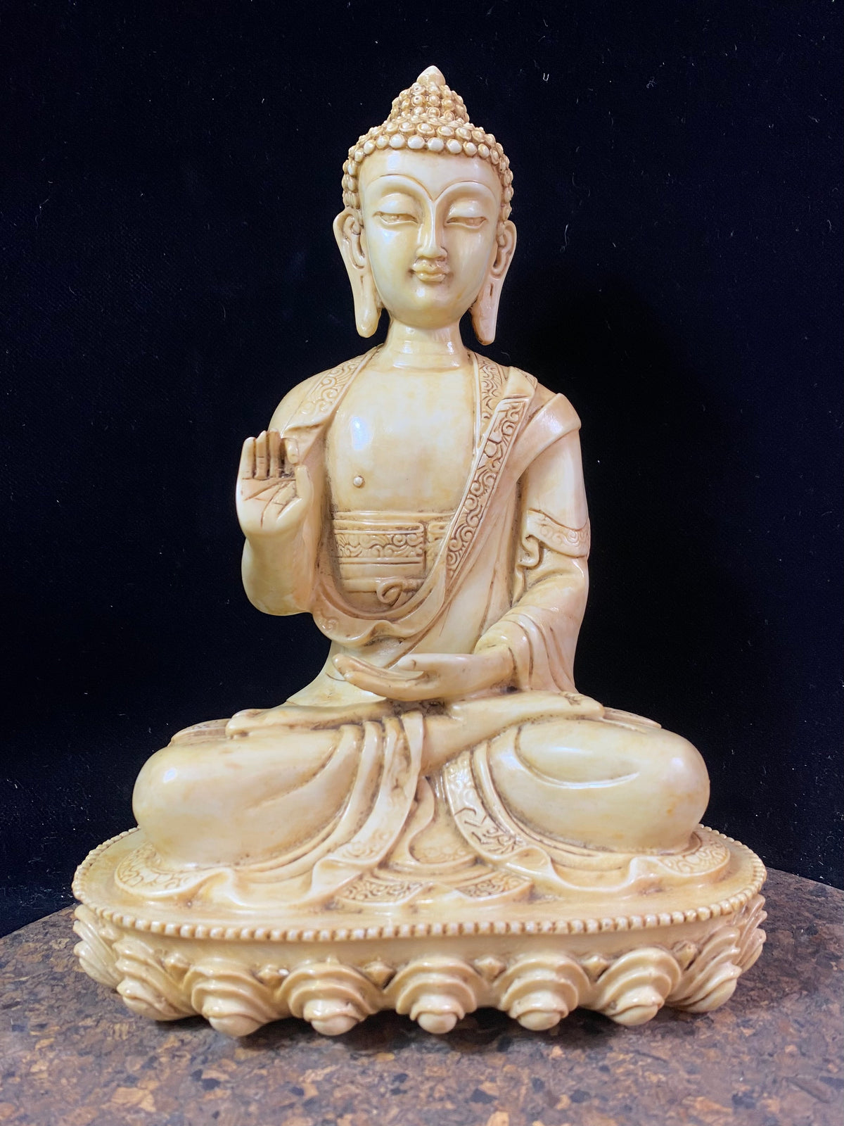Amoghshiddhi Buddha cast in cream coloured resin. His right hand is held up facing outwards in the gesture of protection of fearlessness while his left hand sits in his lap in the gesture of meditation. Cast in solid resin, then hand finished to a very high standard. Measurements: height 26 cm, width 18 cm, depth 12 cm