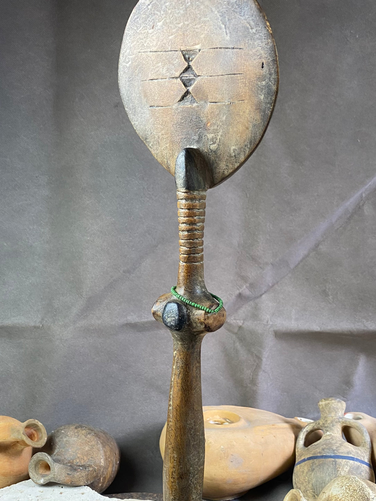 Late 20th Century vintage figure is carved from fine-grained wood, with a natural patina worn smooth with handling. She wears carved neck rings as well as beaded decoration, and a stylised pack on her back. This doll has an well carve face, with other features hinted at rather than explicitly carved. Height 43cm, width at head 11.5 cm.