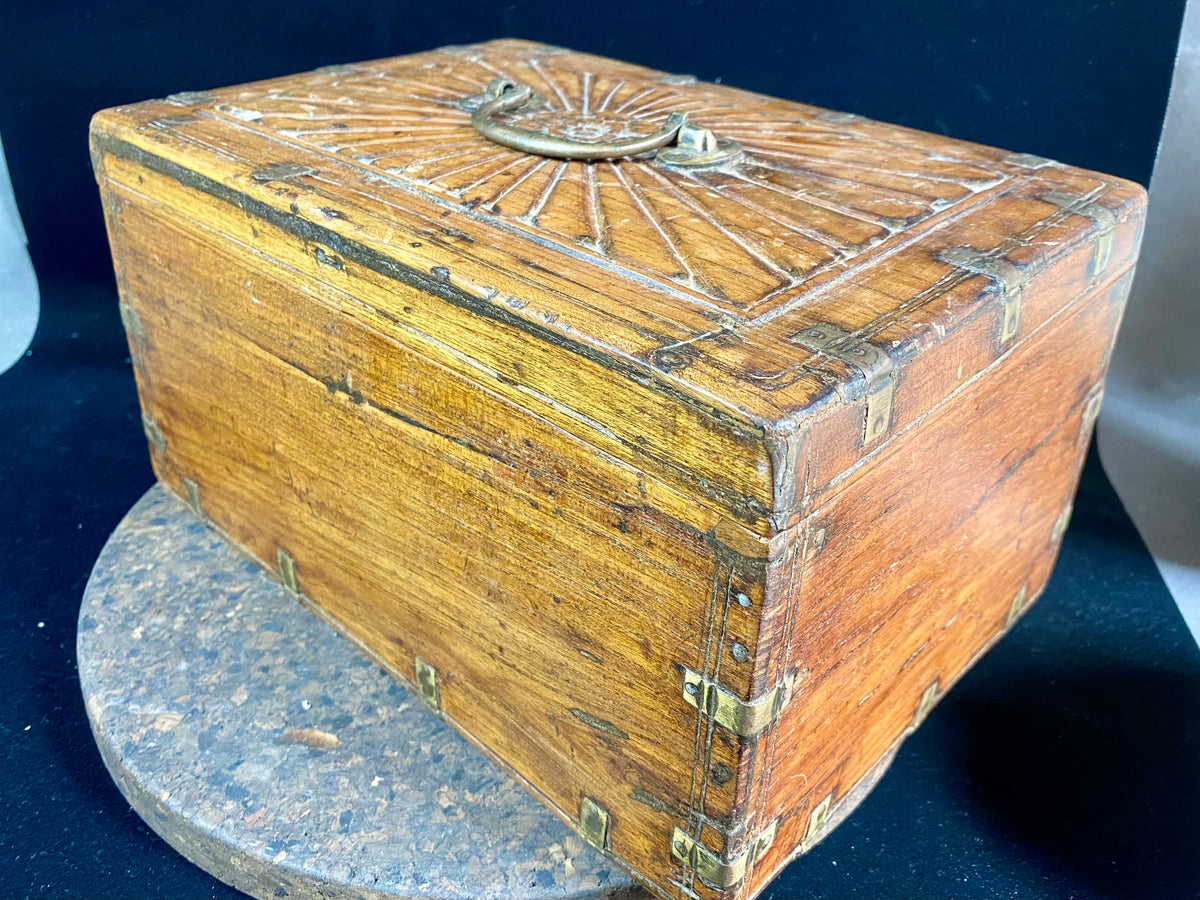A lovely old southern Indian cash box with carved top and original brass trim, handle and hinges. Fitted with two small shelves inside. Made from teak, this would make a lovely trinket box, key box, jewellery, watch or cufflink box Circa 1880 - 1920. Measurements: length 27.5 cm  x depth 19 cm, height 15 cm.