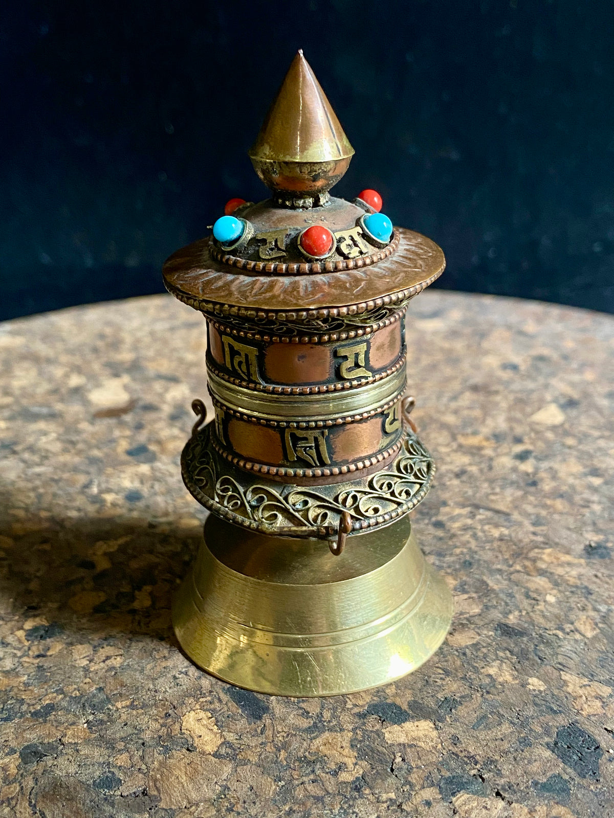 Handmade in Nepal from brass and copper, these small standing prayer wheel are weighted for spinning and contain a scroll on which is printed the mantra "Om Mani Padme Hum", a prayer to the Compassionate Buddha, written many times over. Two styles.  Measurements: height 9 cm