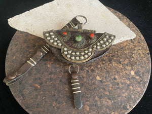 Antique yak leather Tibetan coin purse (mechaks), Mounted on the front with a heavy studded decorative plaque and is inlaid with a real turquoise and two real red coral stones. The metal decoration is a mixture of white metal and brass. Height with strap 36 cm. Purse height 9 cm (including rings), width 14 cm