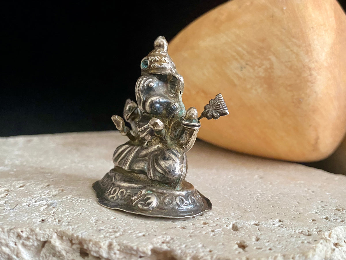 Small vintage Ganesh statue cast in silver, with right hand up in the gesture of protection and left hand holding his favourite ladoo sweet. His other hands hold lotus flowers. Lightweight but very finely cast with a small facet cut blue topaz in his forehead. 50 years old, southern India. 5 cm height