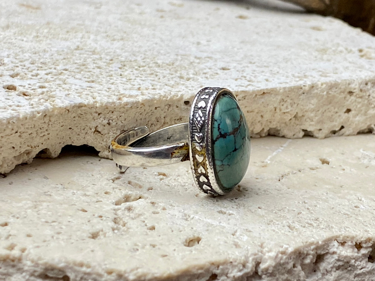 This simple ring features a large antique cabochon turquoise stone, set in a simple patterned silver bezel, with an adjustable ring band. As is the case with many of the rings we are currently buying, the stone is old and has been reset into a new silver band.  Measurements:  Ring face 2 x 1.5 cm Inner diameter 16.5 mm | Size 6 , however the adjustable band will fit any finger sized 5 -7