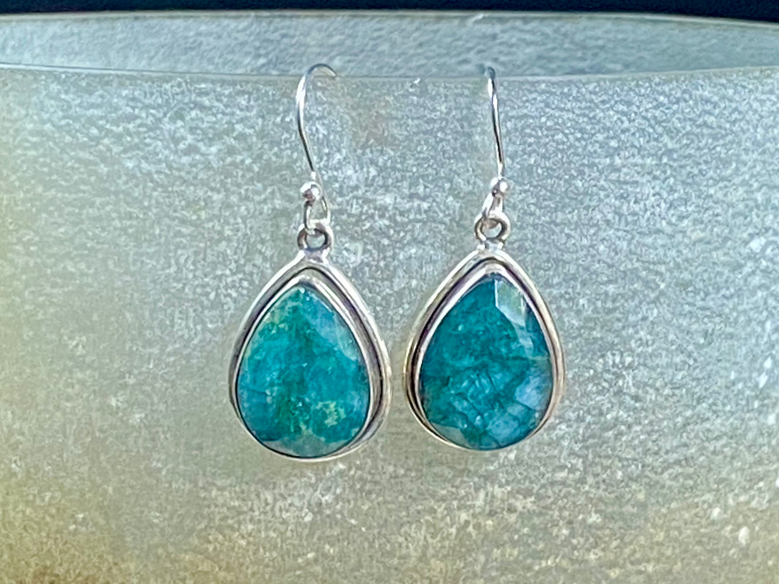 Our beautiful teardrop emerald earrings feature large facet cut emeralds of a deep variegated green colour. They are set in a sterling silver shadow box mount to highlight their beauty. measurements 3.6 cm length including hook.