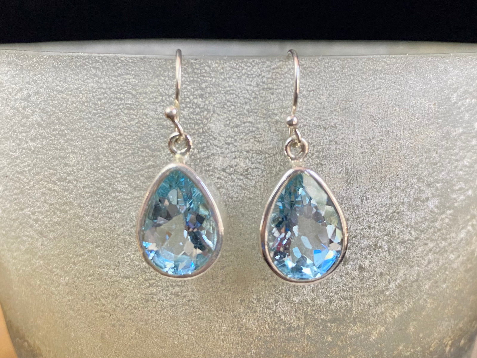 Blue topaz earrings. Deep teardrop cut stones are set in simple silver surrounds and finished with a shepherd hook. The topazes are facet cut to display their excellent quality and sparkle. Measurements: 3 cm height including hook, width 1.1 cm at widest point
