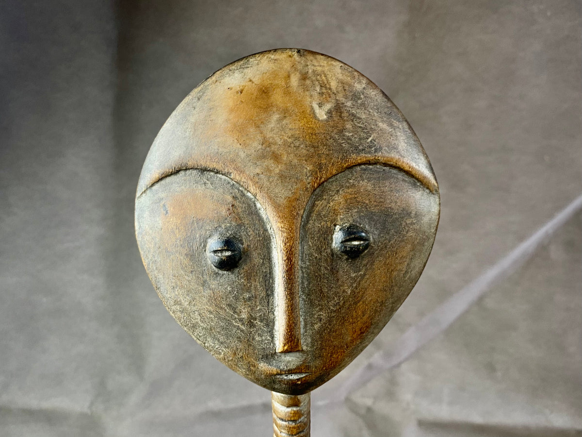 Late 20th Century vintage figure is carved from fine-grained wood, with a natural patina worn smooth with handling. She wears carved neck rings as well as beaded decoration, and a stylised pack on her back. This doll has an well carve face, with other features hinted at rather than explicitly carved. Height 43cm, width at head 11.5 cm.