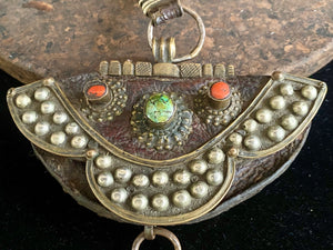 Antique yak leather Tibetan coin purse (mechaks), Mounted on the front with a heavy studded decorative plaque and is inlaid with a real turquoise and two real red coral stones. The metal decoration is a mixture of white metal and brass. Height with strap 36 cm. Purse height 9 cm (including rings), width 14 cm