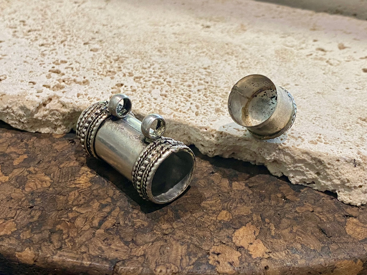 Amulet box or prayer box, these very solid pendants open at one end. Two large bails that even a thick cord or chain will pass through.  White metal.  Length 8 cm, diameter 1.8 cm