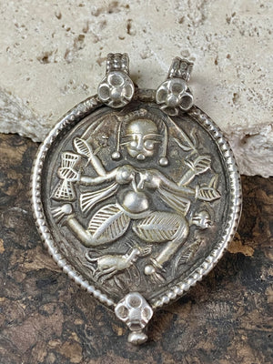 Leaf shaped amulet pendant depicting the goddess Kali. Heavy in silver with a double flower-patterned bail, this is a northern tribal amulet as evidenced by the dog at her feet, associating her with the Bhil people's tribal form of Shiva called Bheru. Early 20th century, northern India. Very high grade silver.  Measurements: total height 5 cm including bail, width 3.5 cm at widest point.