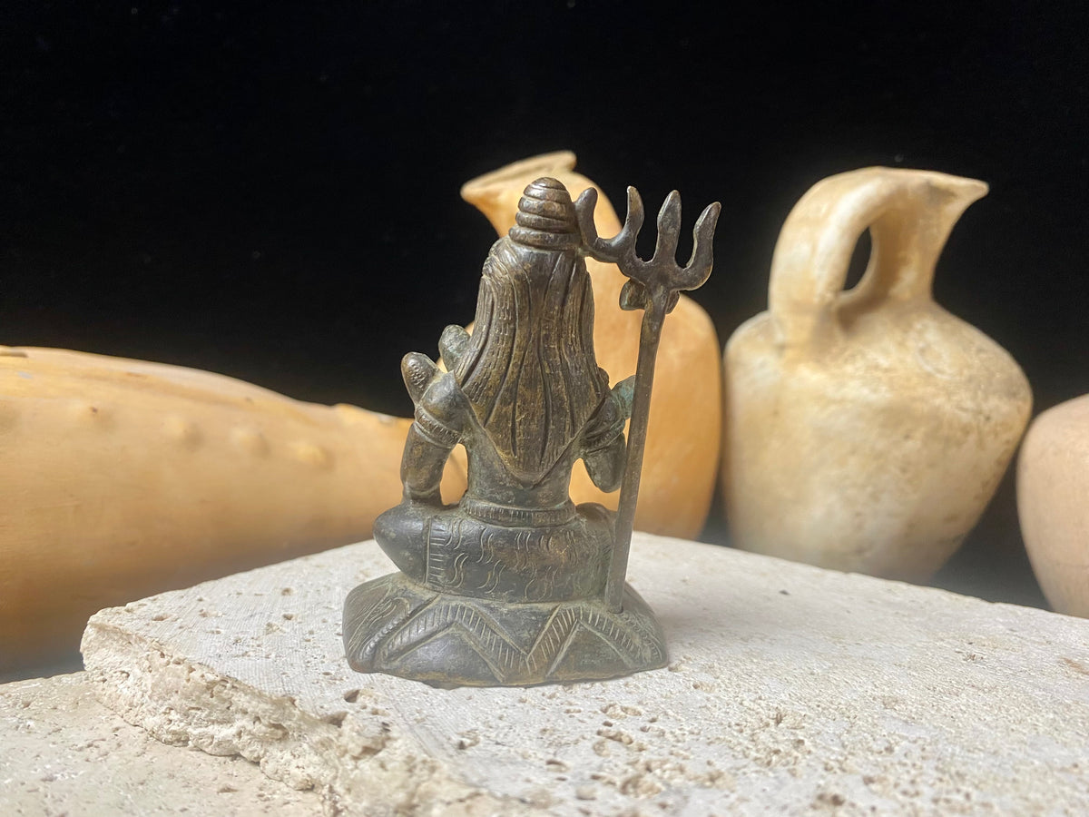 A small cast brass Shiva in serene seated style. This piece has some rubbing on the right hand side of the face and displays softened edges from decades of handling. It has a naturally darkened patina and is approximately 80 years old, or older. Gujarat, India. Measurements: Height 7.7 cm x width 5 cm x depth 3.5 cm