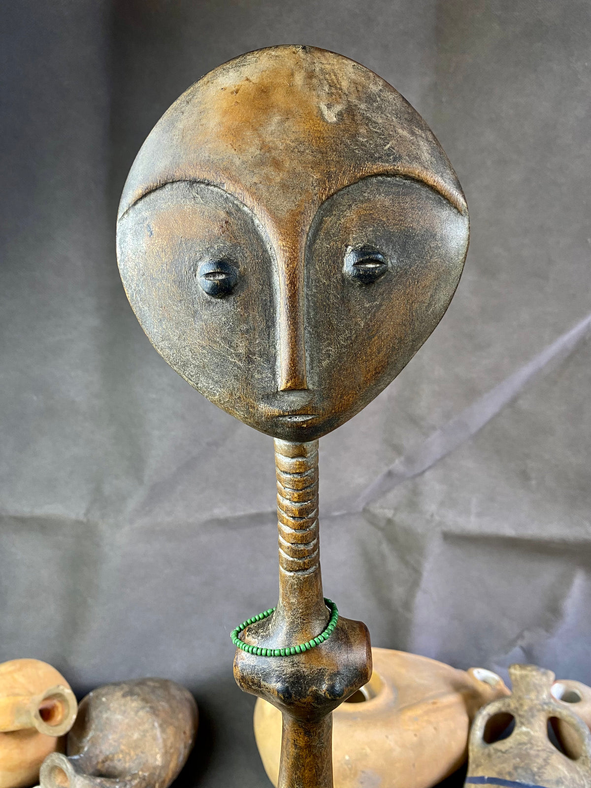 Late 20th Century vintage figure is carved from fine-grained wood, with a natural patina worn smooth with handling. She wears carved neck rings as well as beaded decoration, and a stylised pack on her back. This doll has an well carve face, with other features hinted at rather than explicitly carved. Height 43cm, width at head 11.5 cm.