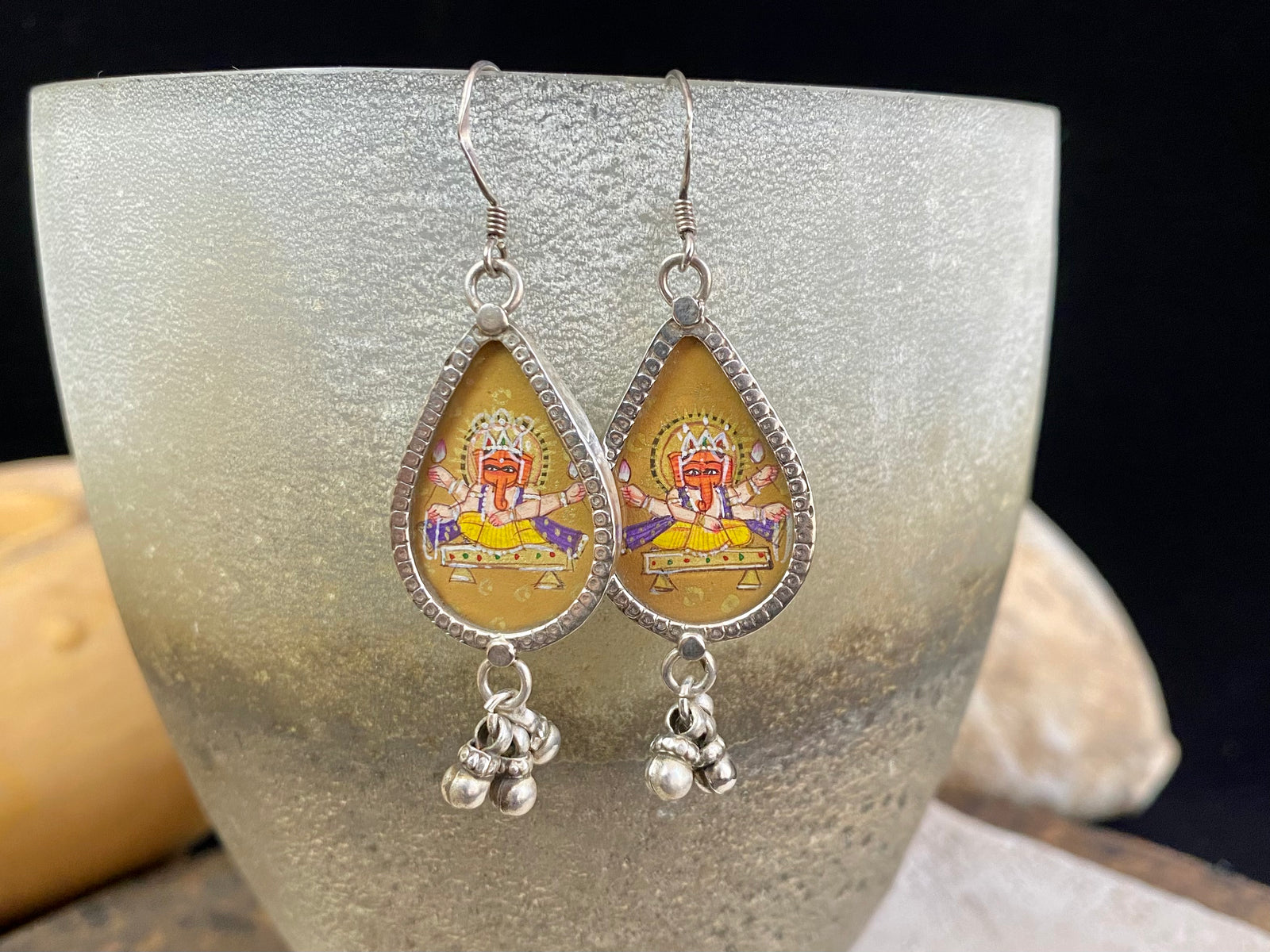 Exquisite miniature hand painted earrings featuring Ganesh seated, set within sterling silver frames, backed with decorated silver and set with a silver dangles bail at the base.  Bought from the artist who painted them in India, then set into silver.  Measurements: 6 cm (2.35") height including hooks or 2 cm at widest point