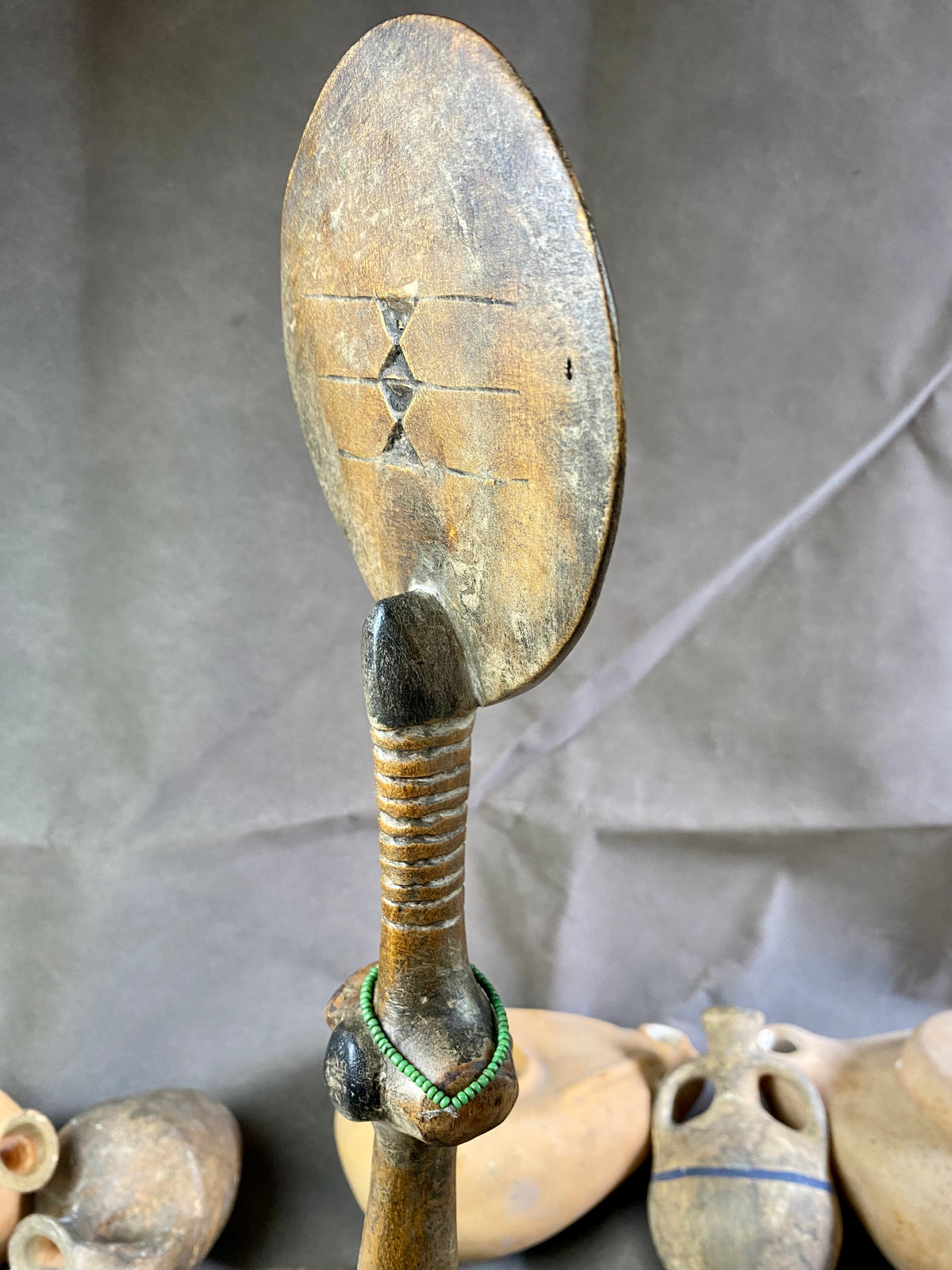 Late 20th Century vintage figure is carved from fine-grained wood, with a natural patina worn smooth with handling. She wears carved neck rings as well as beaded decoration, and a stylised pack on her back. This doll has an well carve face, with other features hinted at rather than explicitly carved. Height 43cm, width at head 11.5 cm.