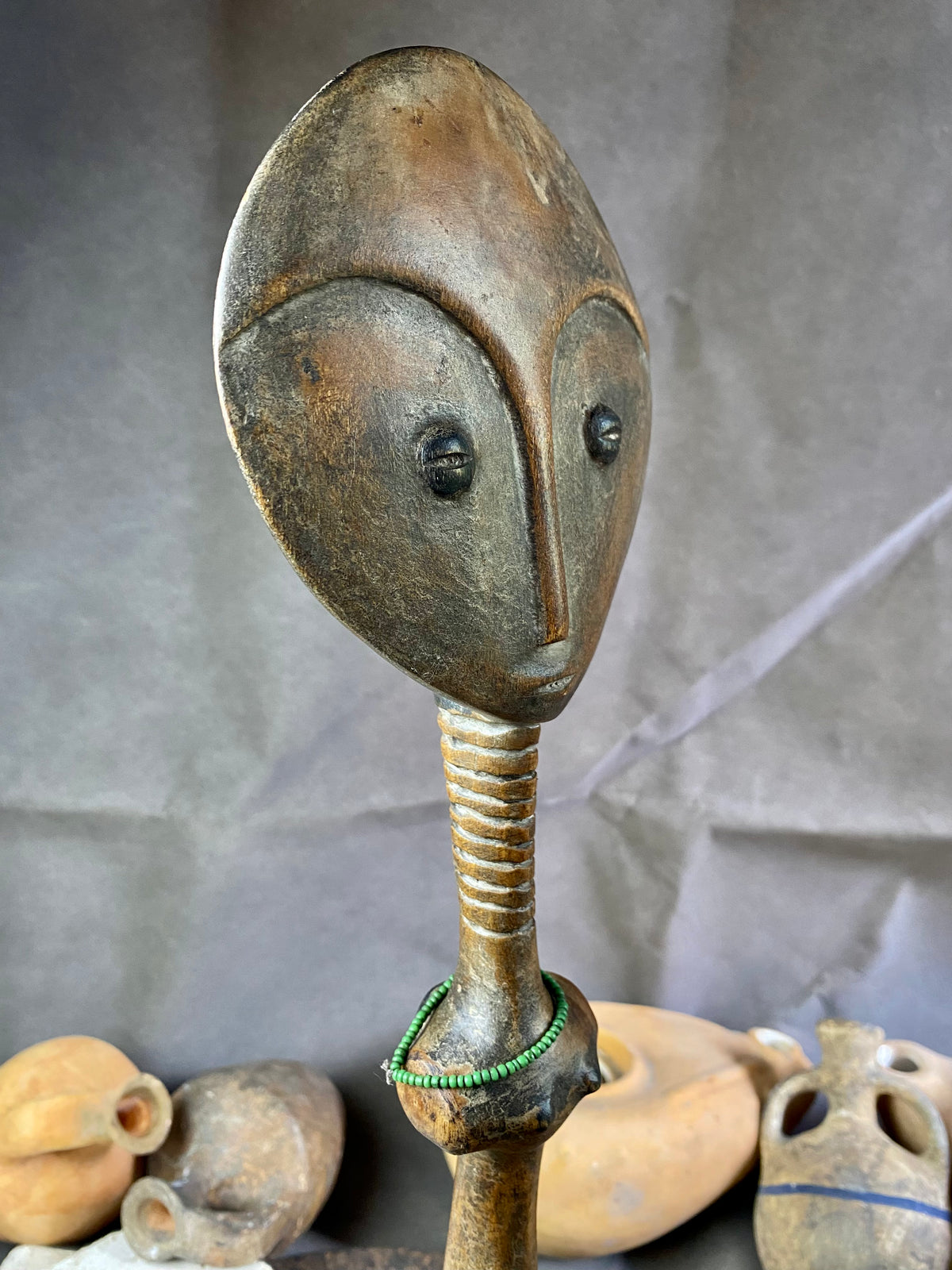 Late 20th Century vintage figure is carved from fine-grained wood, with a natural patina worn smooth with handling. She wears carved neck rings as well as beaded decoration, and a stylised pack on her back. This doll has an well carve face, with other features hinted at rather than explicitly carved. Height 43cm, width at head 11.5 cm.