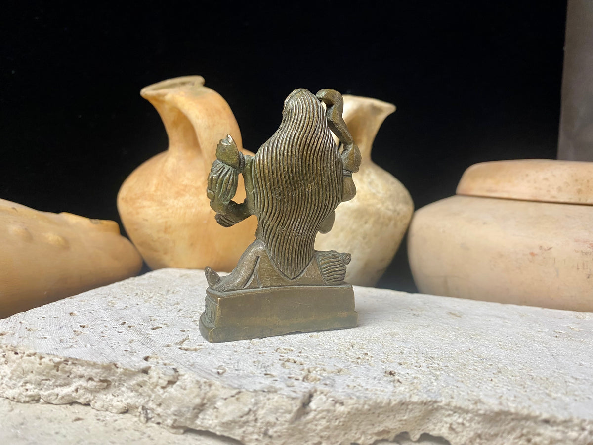 Kali with four arms, standing on Shiva, holding a curved sword, severed head and skull cup. Her fourth hand displays the gesture of blessing. She wears a garland of skulls around her neck and is covered by her long, wild, disheveled hair. This statue is approximately 80 years old (early 20th century). She has a fine and evenly dark patina.  Measurements: height 7.3 cm, width 5 cm.