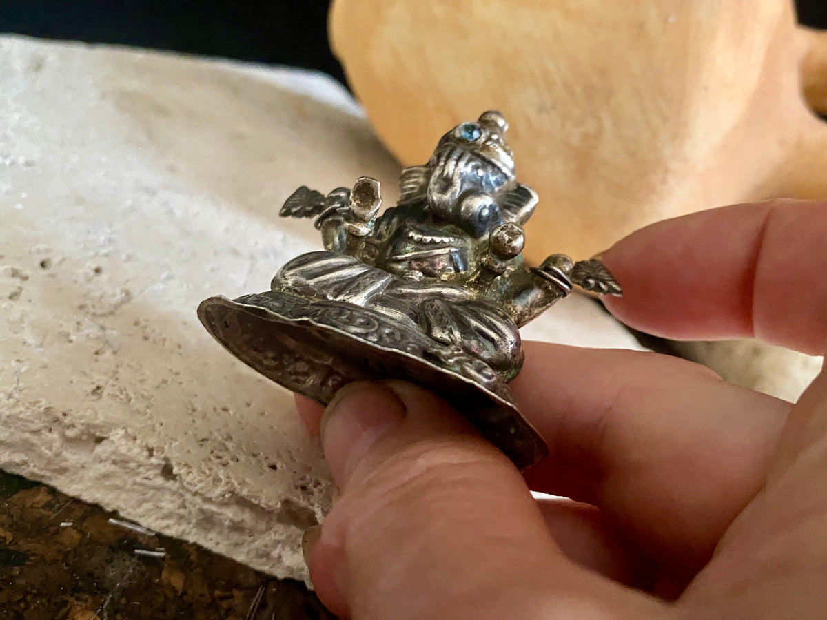 Small vintage Ganesh statue cast in silver, with right hand up in the gesture of protection and left hand holding his favourite ladoo sweet. His other hands hold lotus flowers. Lightweight but very finely cast with a small facet cut blue topaz in his forehead. 50 years old, southern India. 5 cm height